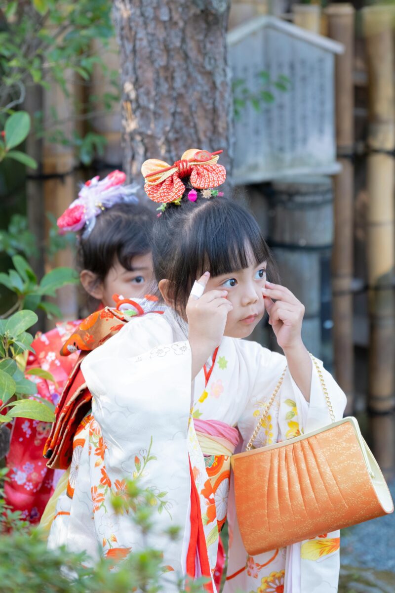Dievčatká v tradičných japonských kimono pózujú v záhrade, zdobené farebnými doplnkami.