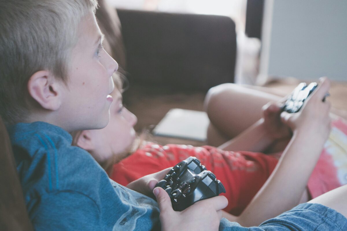 Deti hrajú videohry na gauči s ovládačmi v ruke, domáca zábava a relax.