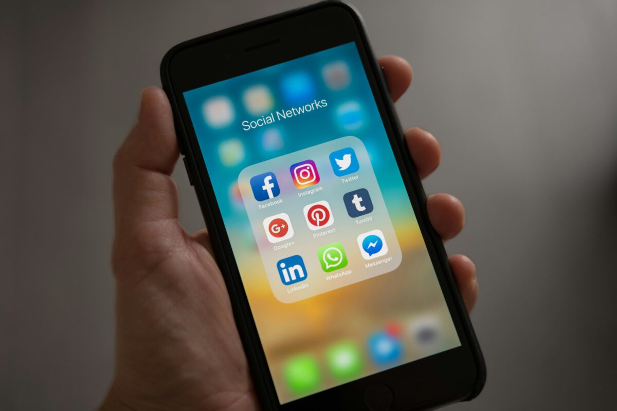 Ruka držiaca mobil s ikonami sociálnych sietí, vrátane Facebooku, Instagramu a Twitteru, na hlavnej obrazovke telefónu.