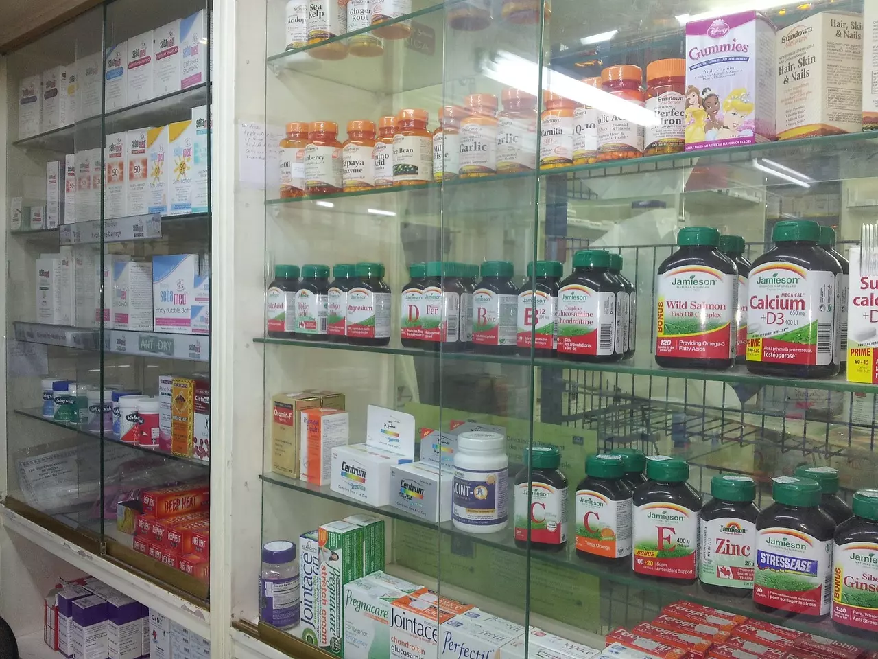 Sklenené police plné vitamínových doplnkov a zdravotných produktov v lekárni.