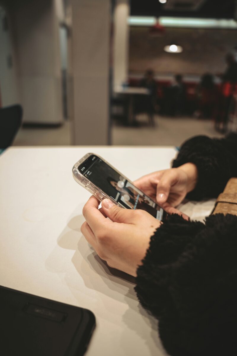 Osoba držiaca smartfón v ruke a prezerajúca si obsah v kaviarni.