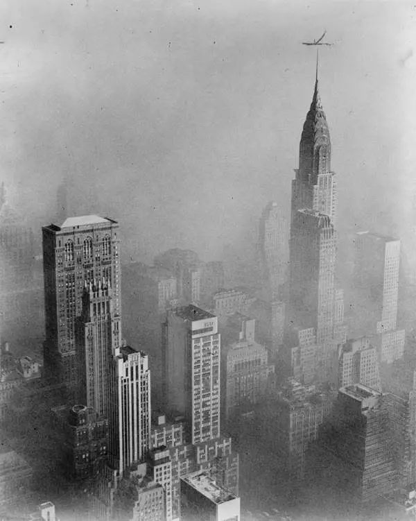 Historický pohľad na mrakodrapy New Yorku s ikonickou siluetou Chrysler Building zahalenou v hmle, lietadlo nad mestom.