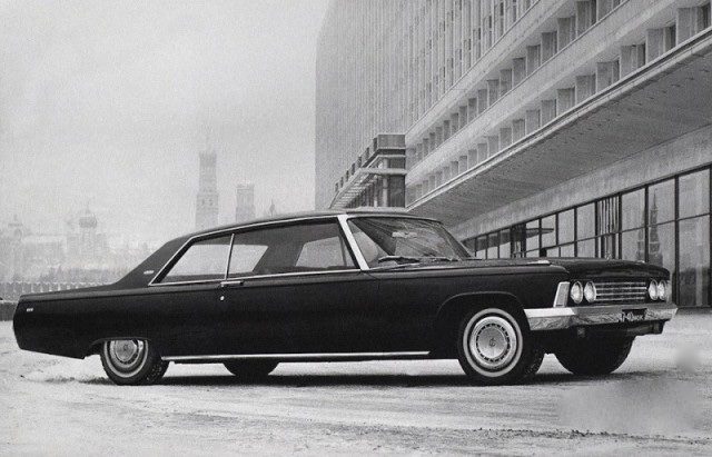 Čierne vintage auto zaparkované vedľa modernej budovy s historickými vežami v pozadí.