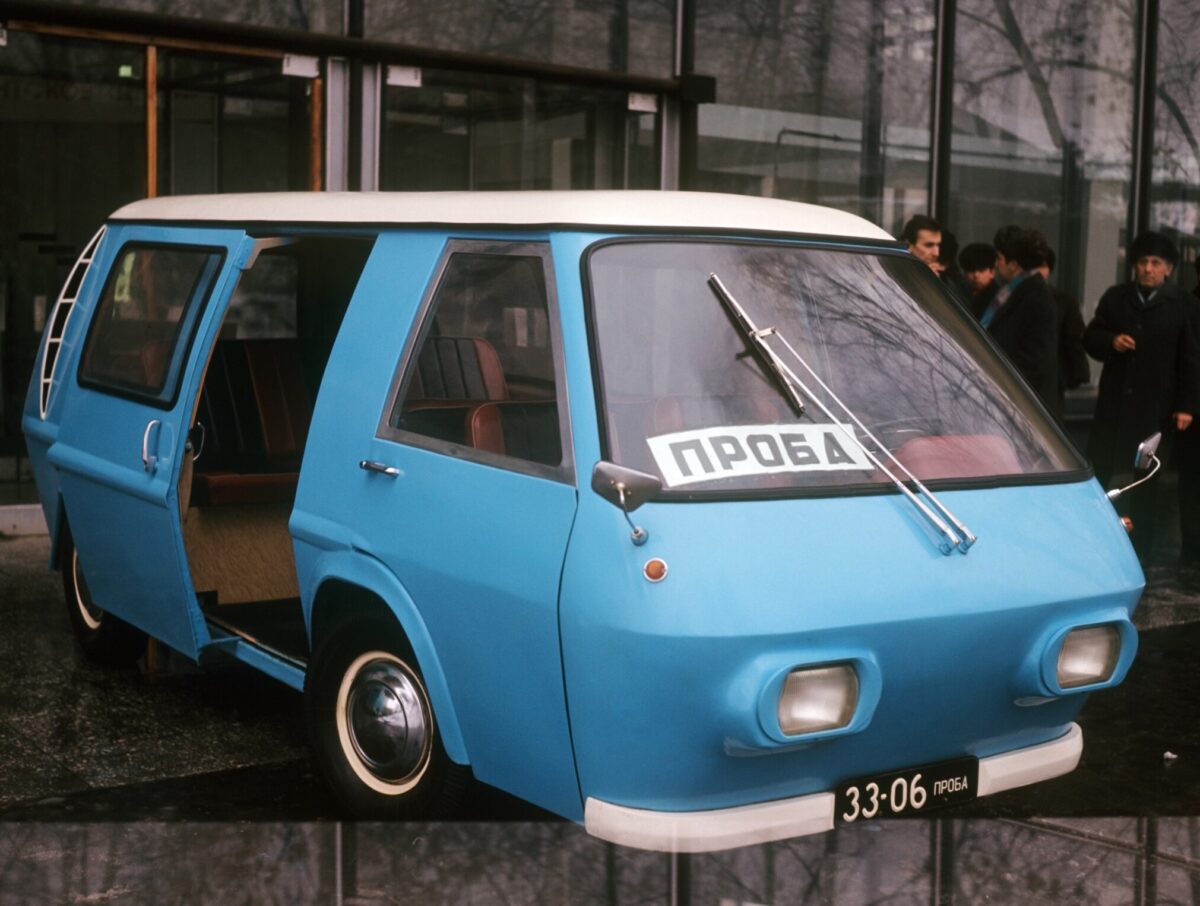 Modrý retro mikrobus s otvorenými dverami pred budovou, znak ПРОБА na čelnom skle.