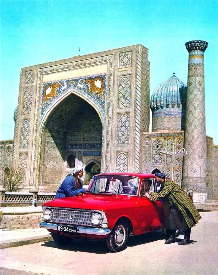 Červené auto pred historickou stavbou s klenutým vstupom a ozdobnými dlaždicami na pozadí.