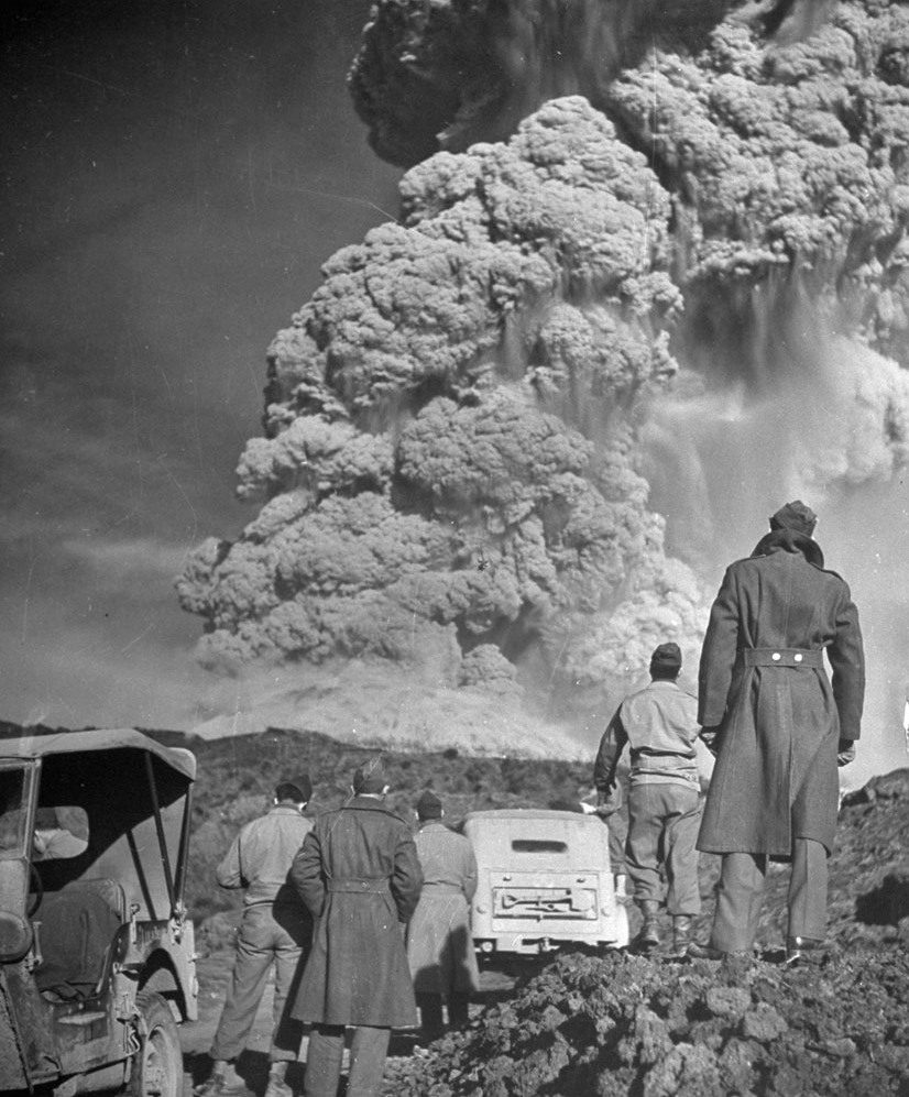 Ľudia sledujúci mohutnú erupciu sopky, obklopení dymom a popolom, historický moment prírody v akcii.