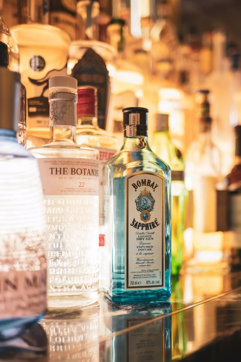 Fľaše ginu na osvetlenej polici v bare, vrátane značiek Bombay Sapphire a The Botanist.