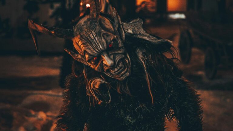 Krampus v tradičnom kostýme s červenými očami počas nočnej zimnej slávnosti.