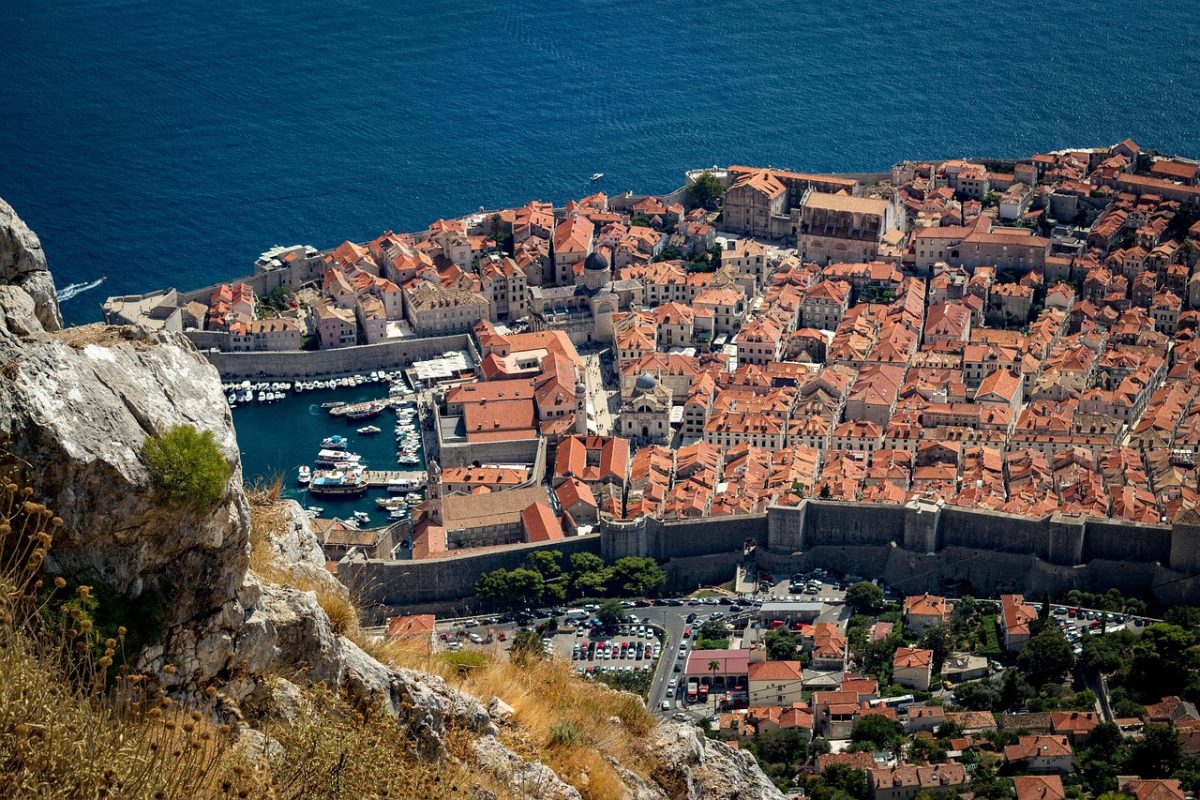 Letecký pohľad na historické centrum Dubrovníka s červenými strechami a prístavom pri Jadranskom mori.