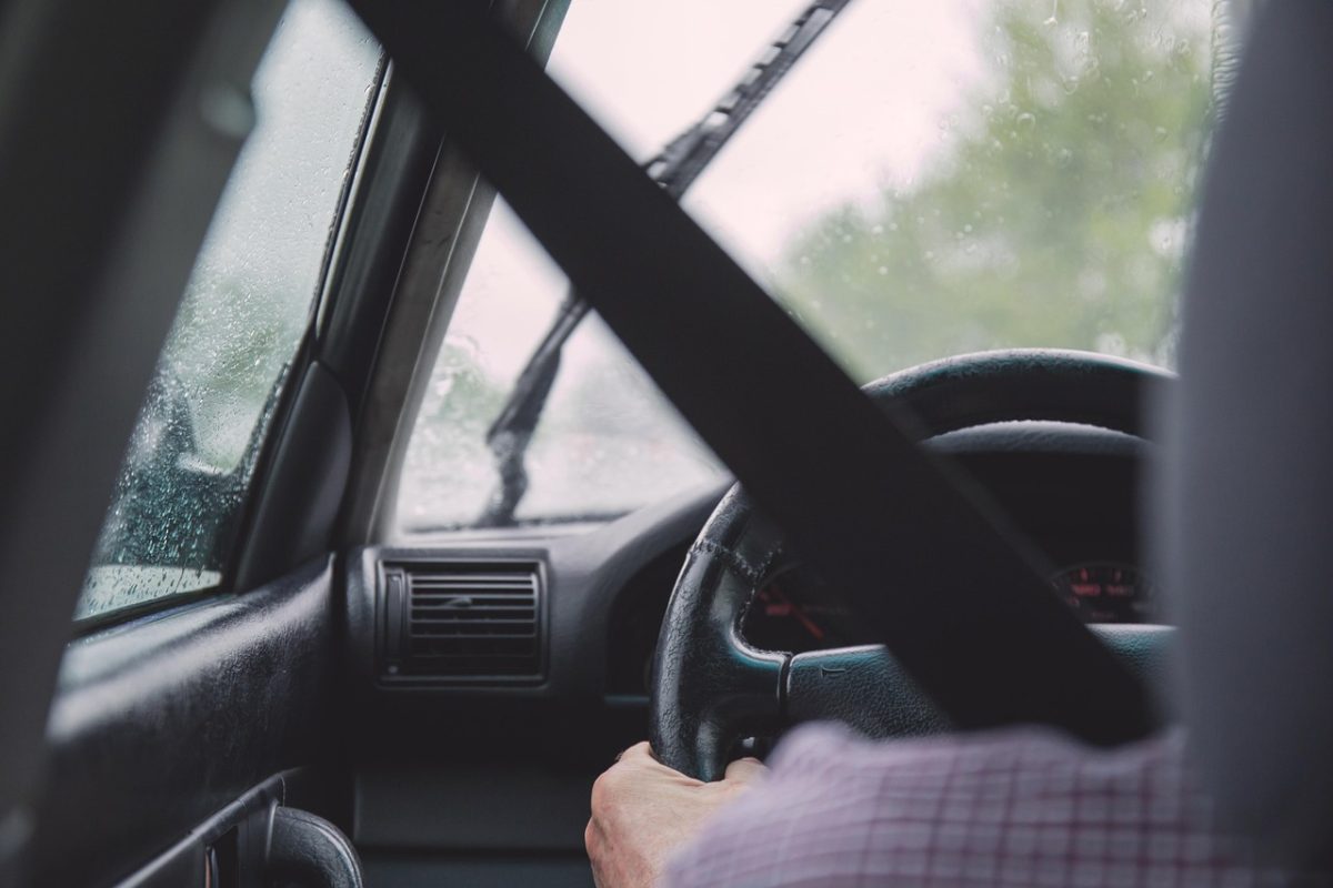 Šofér riadi auto počas dažďa, zapnutý bezpečnostný pás a aktivované stierače, dôraz na bezpečnosť jazdy.