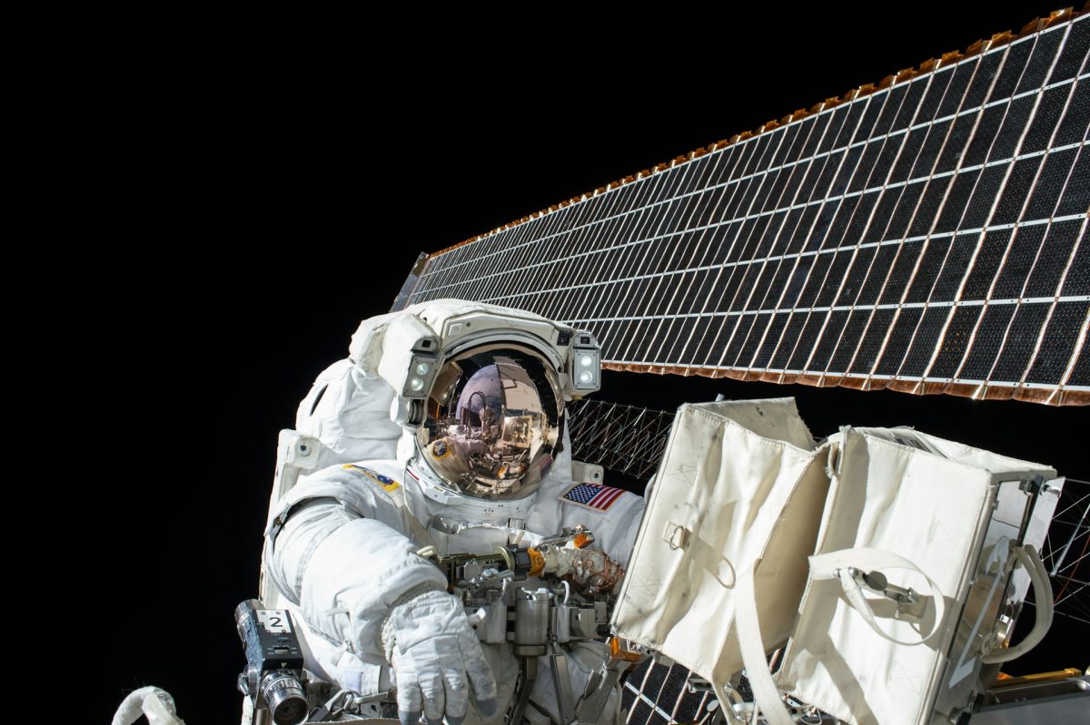 Astronaut v skafandri pracujúci na údržbe vesmírnej stanice pred solárnym panelom na obežnej dráhe Zeme.