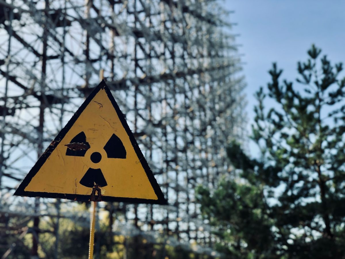 Rádioválogná značka pred gigantickou kovovou konštrukciou a stromami, pod jasnou oblohou.