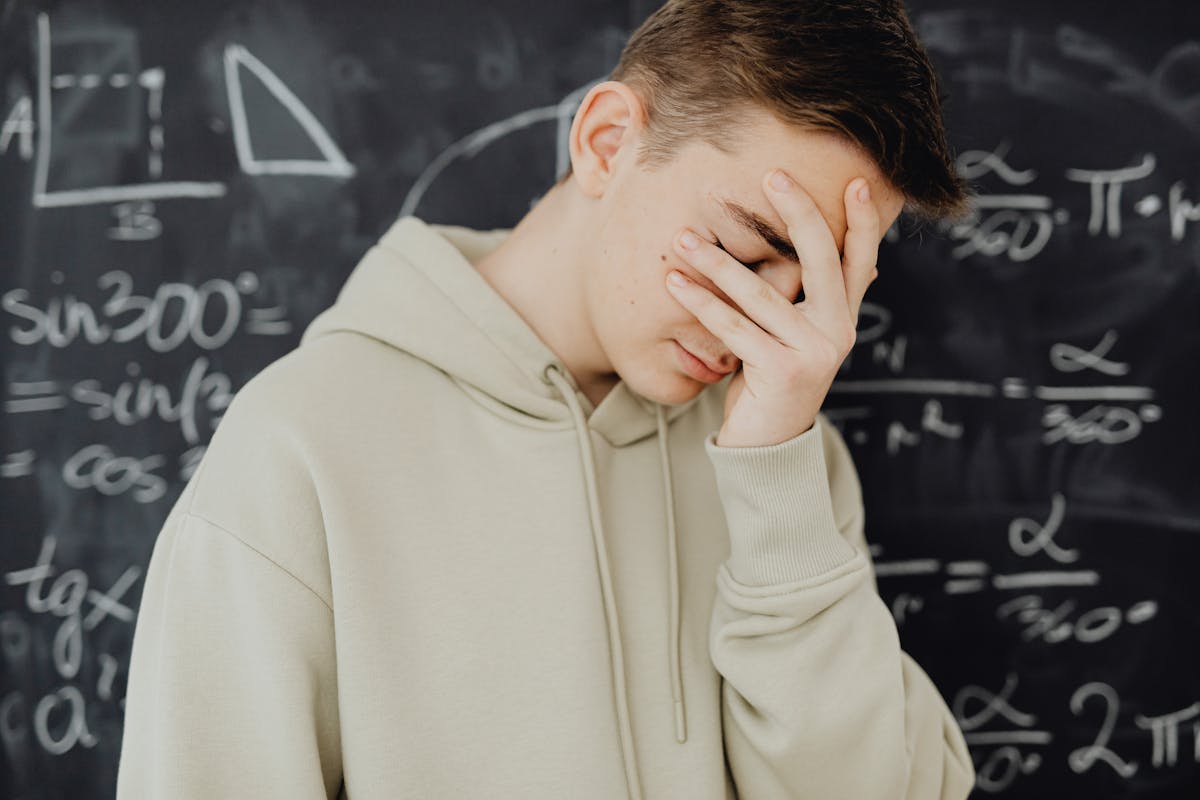 Young man overwhelmed by mathematical calculations on a blackboard in a classroom setting.